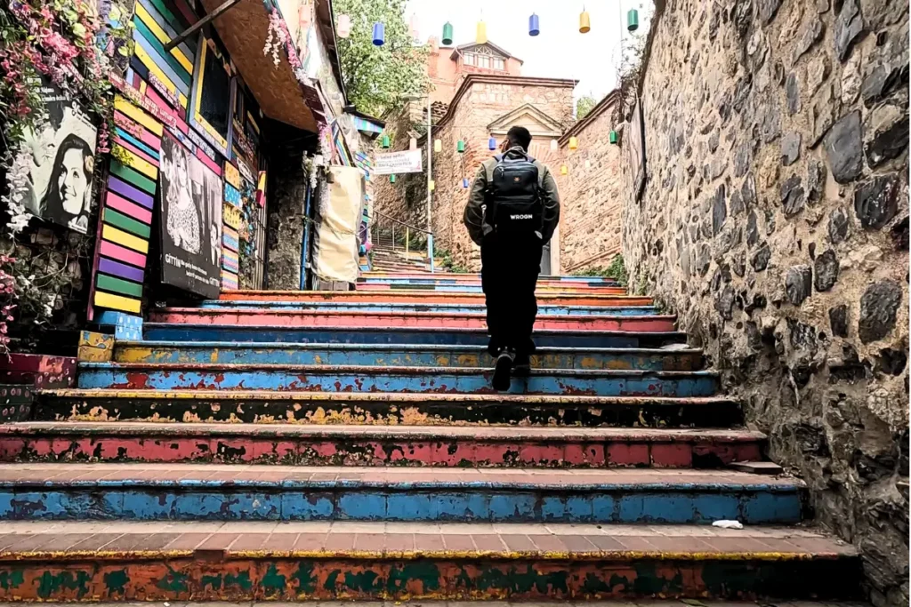 Istanbul- Balat-3 Akash walking up a colorful outdoor stone staircase painted in bright rainbow shades, flanked by historic masonry walls in Balat.