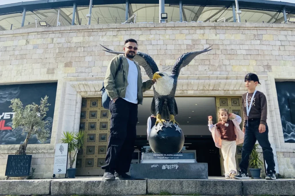 Istanbul- Besiktas- The Black Eagles Akash posing next to a large black eagle statue mounted on a decorative pedestal outdoors.