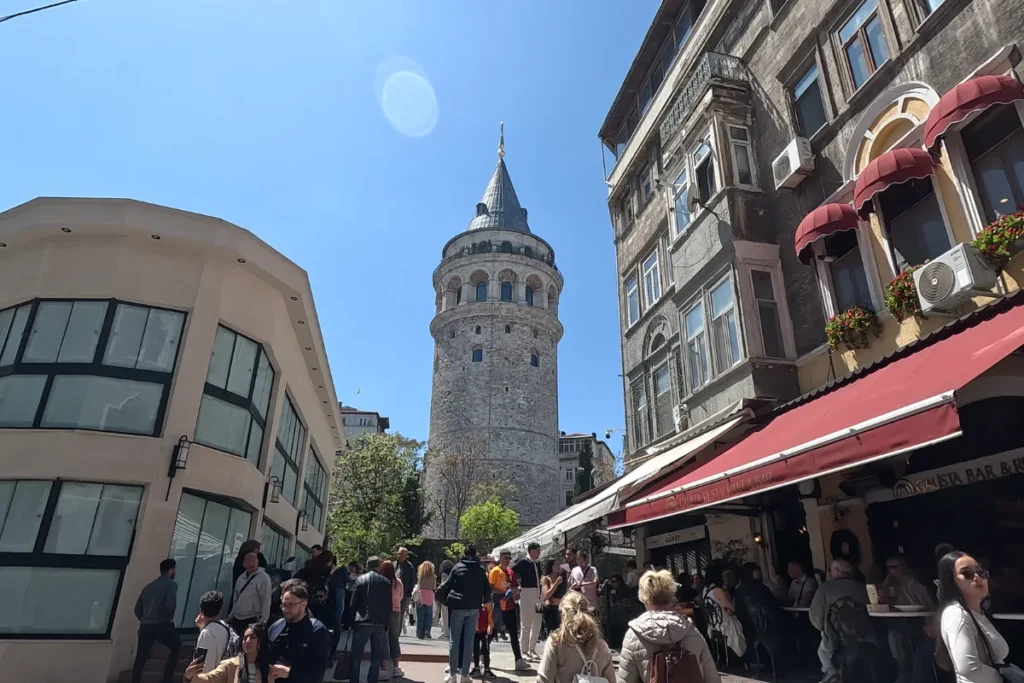 Istanbul- Galata Tower-daytime A daytime view looking up a narrow street crowded with pedestrians and outdoor restaurant seating leading toward the Galata Tower.