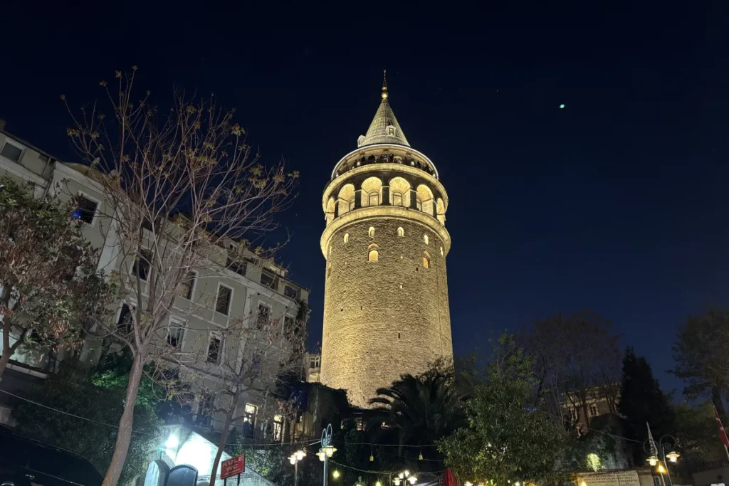 Istanbul- Galata Tower evening The historic stone Galata Tower beautifully illuminated under a deep twilight sky, towering over a crowded street.