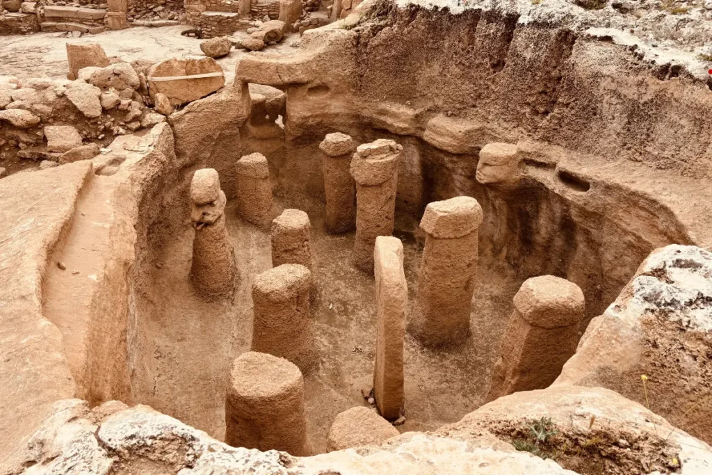 The excavated archaeological site of Karahan Tepe showing early-stage stone pillars carved directly into the bedrock under a white canopy shelter.