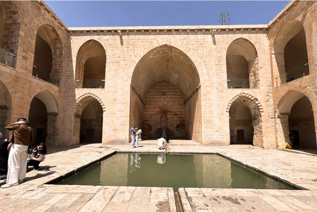 A central courtyard with a large rectangular reflection pool surrounded by two-story stone arcades at the Kasimiye Madrasa.