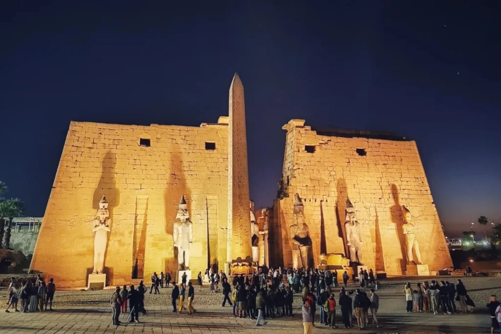 A long row of towering papyrus-bud columns lit up at night inside Luxor Temple.