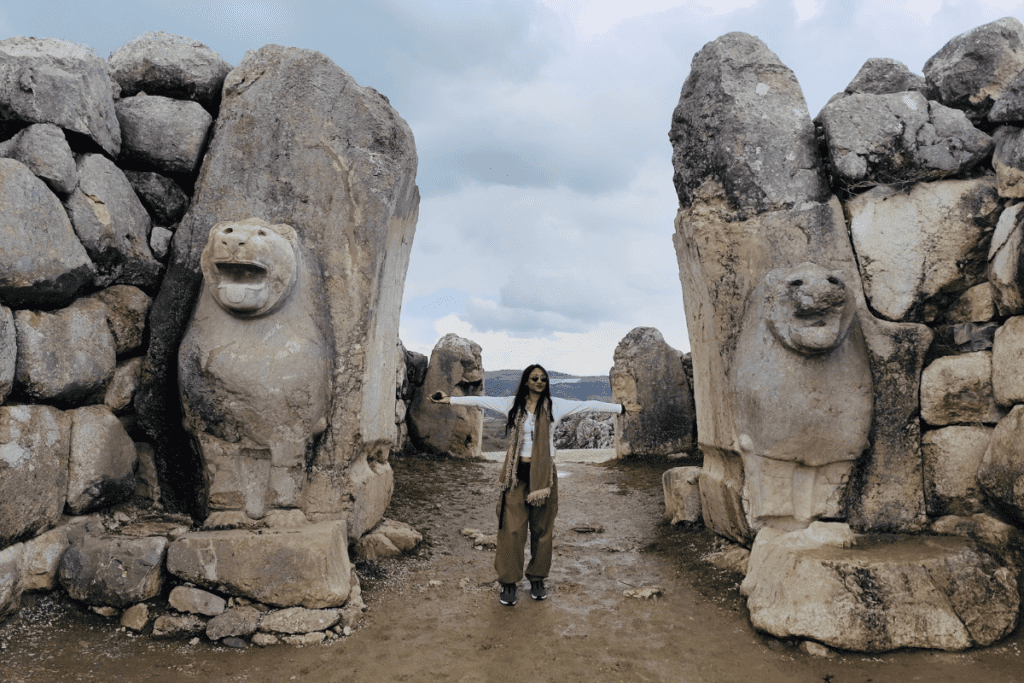 Sumana standing between two massive, ancient stone monoliths carved with lion imagery.