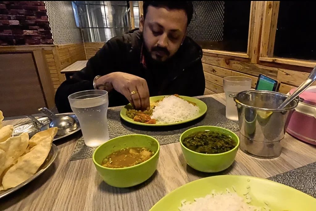 A collection of small steel bowls containing various curries, sambar, and chutneys served on a large banana leaf inside a restaurant.