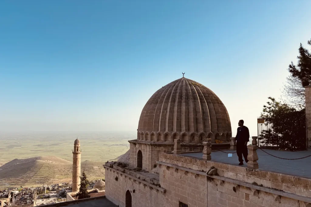The grand stone dome and minaret of the Zinciriye Medresesi overlooking the sprawling city of Mardin at dusk.