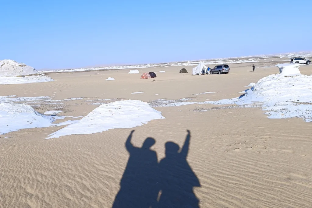 The shadows of two people making peace signs cast longly onto the textured surface of a white limestone rock.