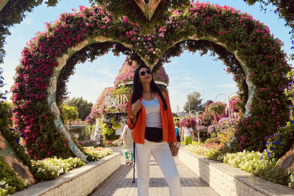 Sumana standing under a series of monumental, heart-shaped floral arches lining a pathway inside the Dubai Miracle Garden.
