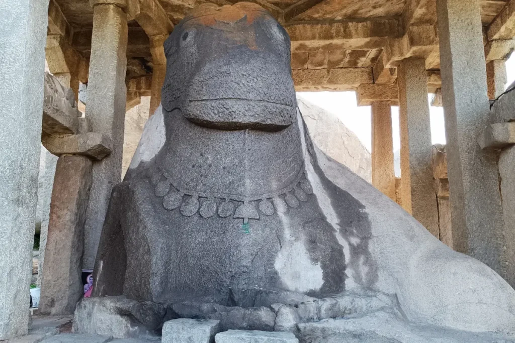A large, ancient monolithic stone statue of the Nandi bull housed inside an open-fronted stone mandapa pavilion.