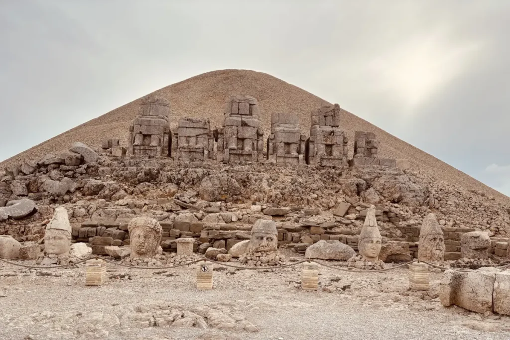 The monumental East Terrace of Mount Nemrut showing a row of large, seated stone statues sitting on thrones in front of a giant gravel tumulus mound.