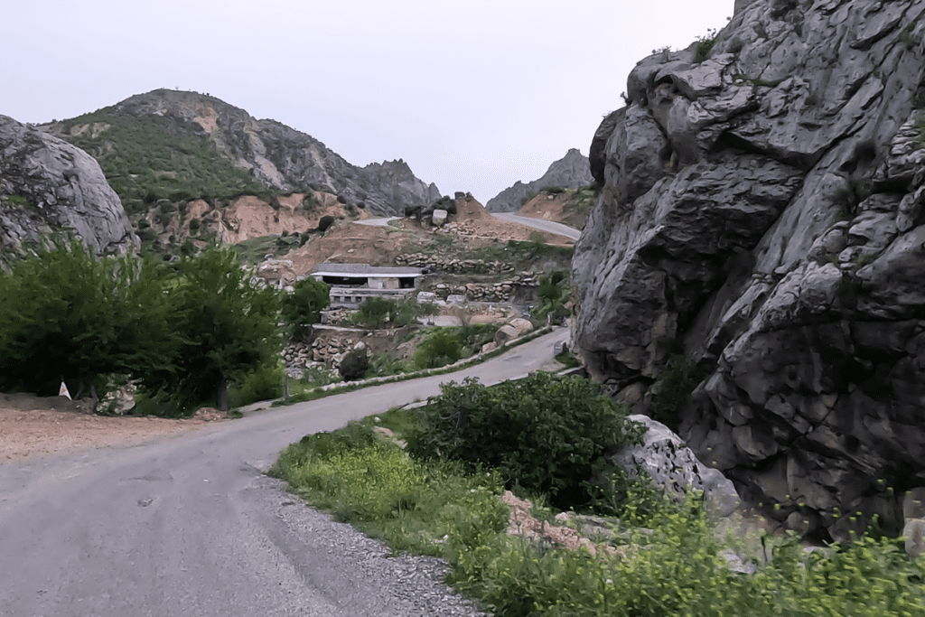 A high-altitude asphalt road winding along a rugged, steep mountain ridge with deep valleys below.