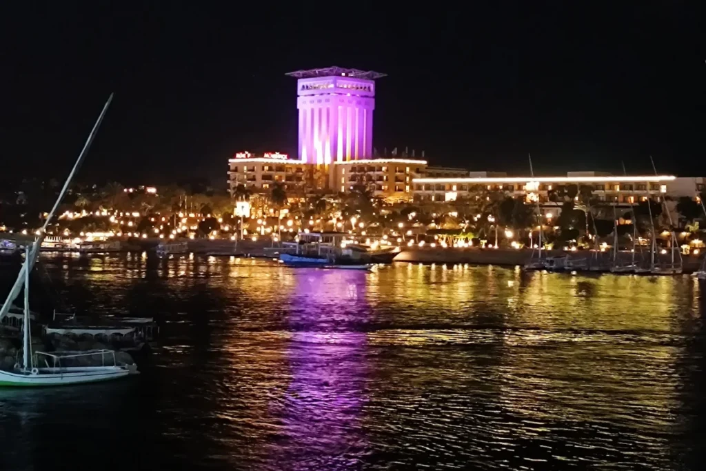 A city skyline illuminated at night across the dark waters of the Nile River.