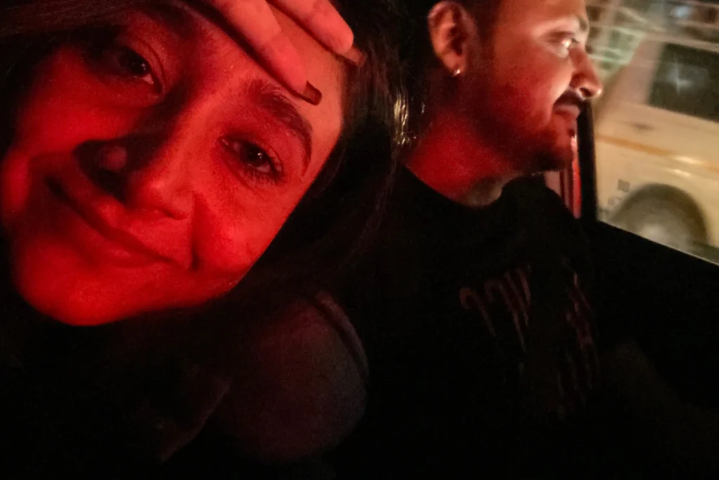 A close-up selfie of Akash & Sumana smiling warmly inside a dimly lit car cabin at night.
