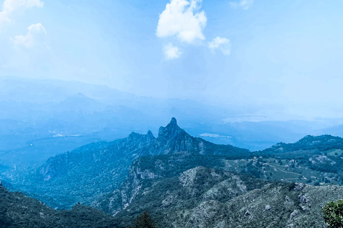 A wide view of sharp, rugged mountain peaks and ridges stretching across the horizon under a hazy blue sky.