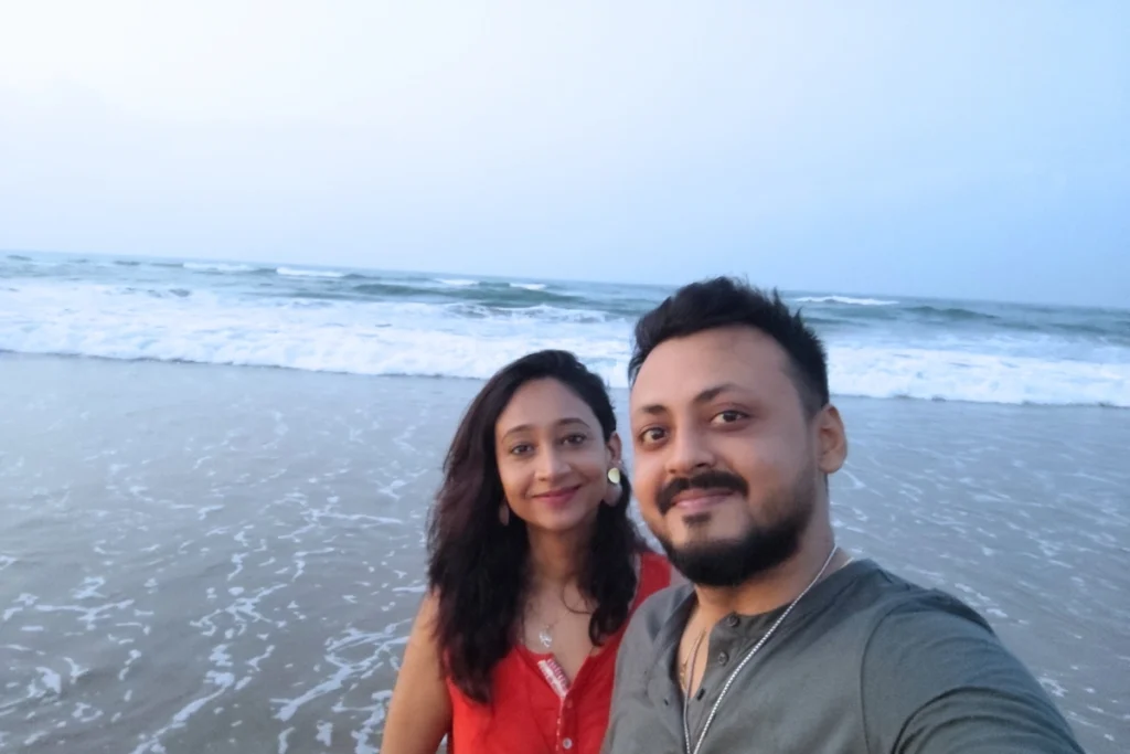A selfie of Akash & Sumana smiling together with sea in the background.