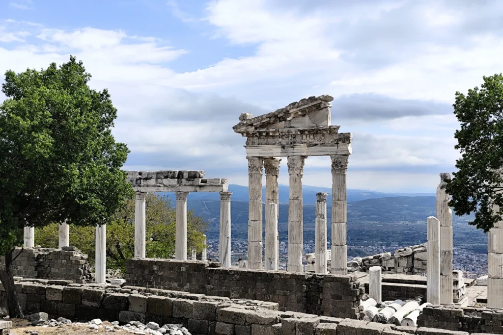 Ruined stone pillars and temple foundations standing on a grassy hill overlooking a town below.