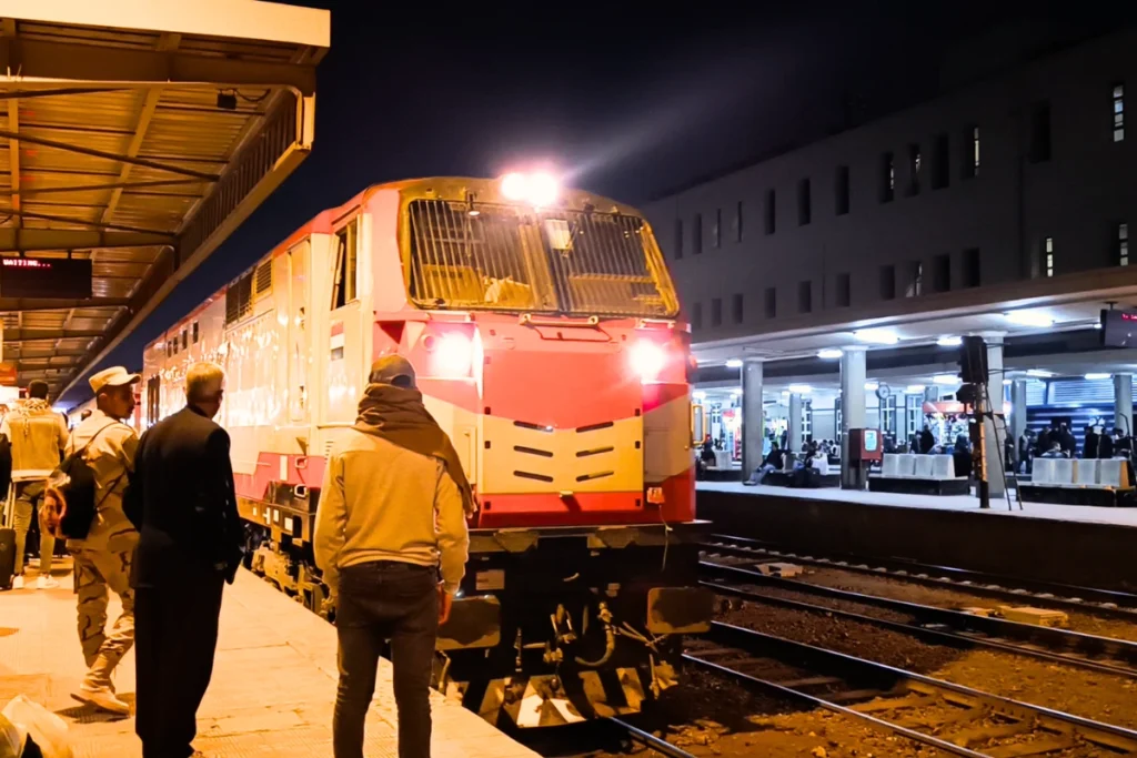 People waiting at a busy train platform alongside a waiting passenger train.
