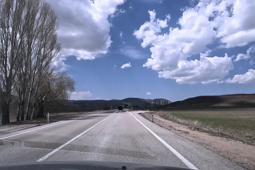 A rural, winding two-lane paved highway cutting through dry, rocky desert terrain under a bright blue sky.