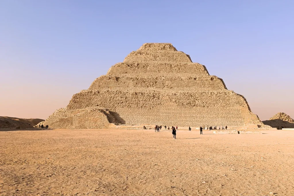 A wide shot of the ancient, multi-tiered Step Pyramid of Djoser at Saqqara against a clear sky.