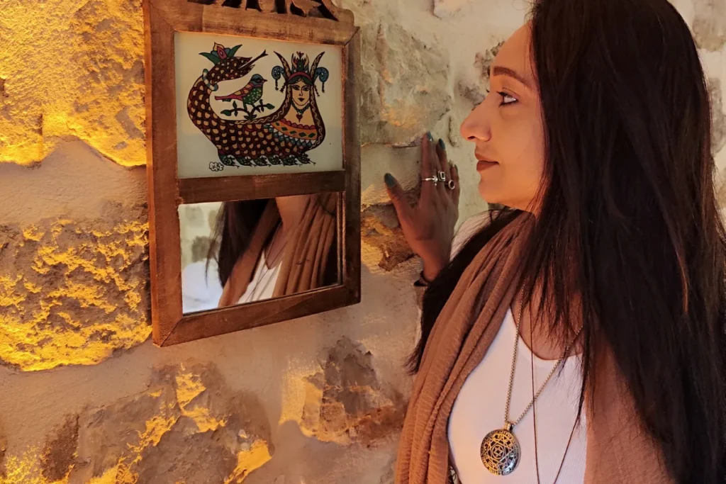 Sumana profile view, looking at a framed painting of Shahmaran hanging on a stone wall.