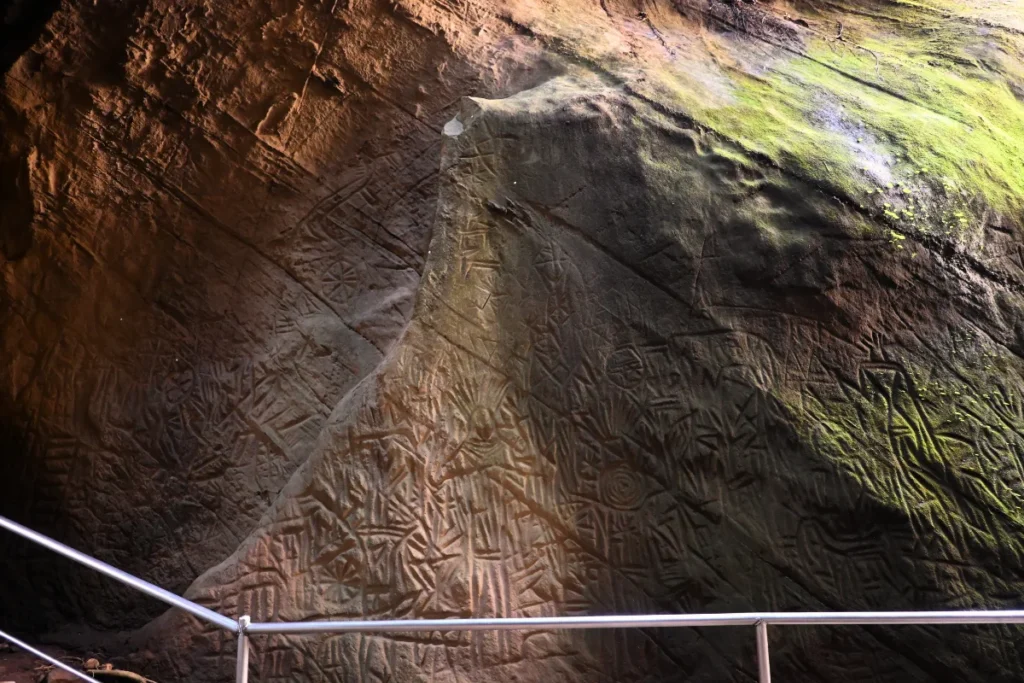 South India- Edakkel Cave 3 Detailed rock carvings showing geometric shapes, human figures, and symbols etched onto a weathered cave wall.