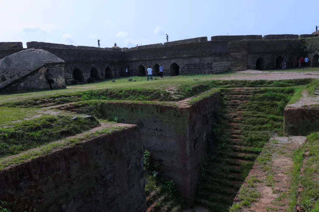 South India- Manjarabad Star Shaped Fort An interior view of Manjarabad Fort in Karnataka, showing moss-covered stone steps leading into a deep central pit, surrounded by green lawns and the fort's stone ramparts under a clear sky.