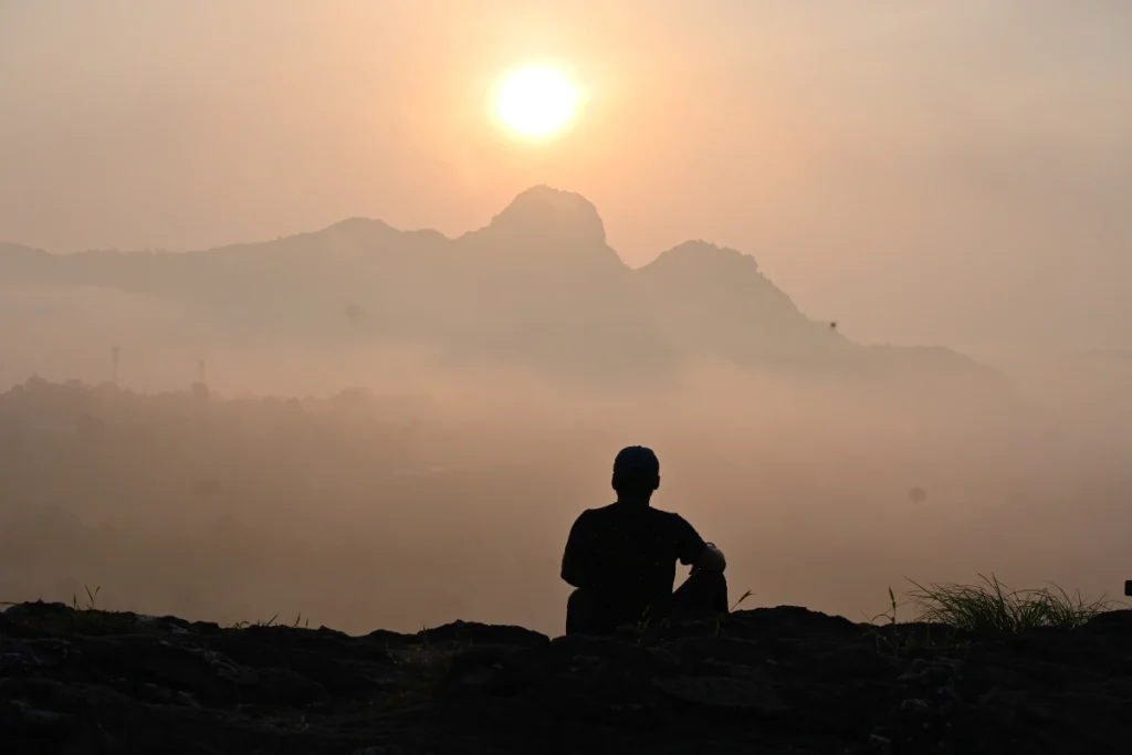South India- Manjarappa sunrise The silhouette of Akash sitting on top of a rocky hill against a soft, gradient sky during sunrise.