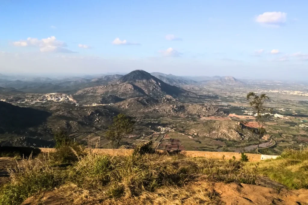 South India- Nandi Hills 1 A high-angle, wide panoramic shot looking down onto a sprawling plain, farmlands, and small villages from a mountain peak.