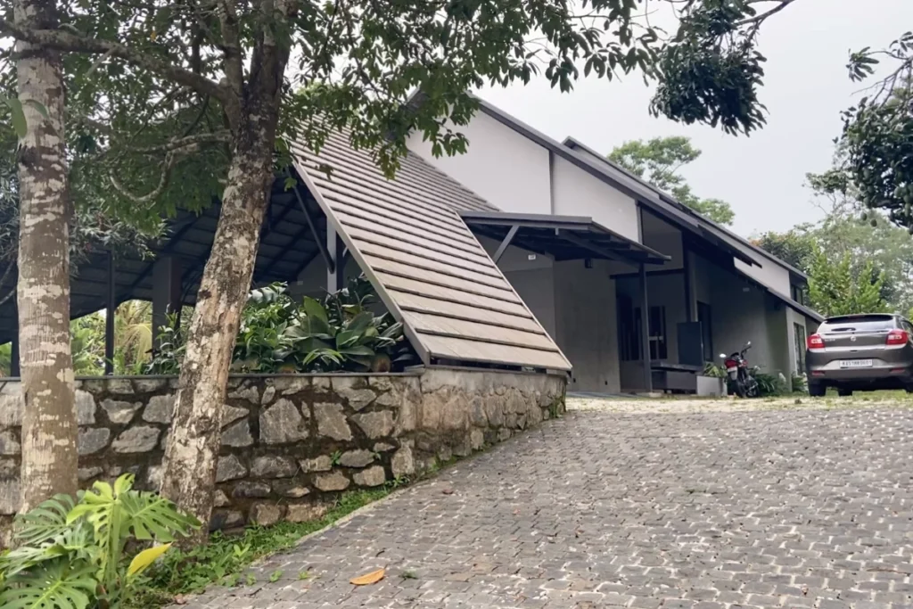 South India- Wayanad Stay 1 A modern, single-story house with a unique stone-textured front wall and a small green lawn.