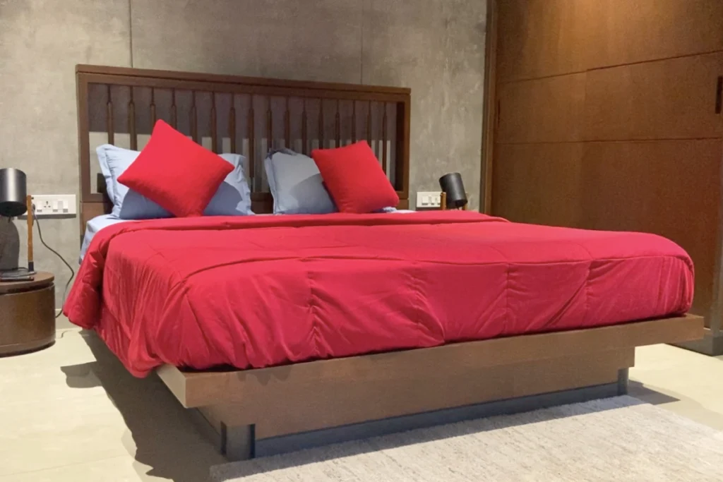 South India- Wayanad Stay 2 An interior shot of a minimalist bedroom featuring a neat bed with a plush burgundy comforter.