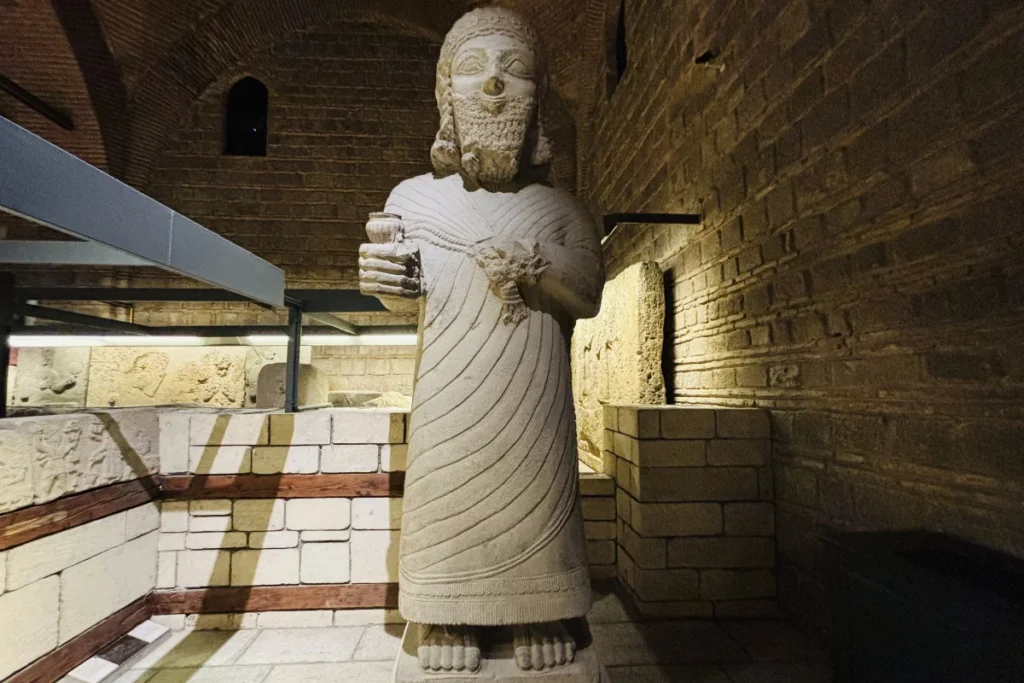 A tall, carved limestone statue of King Mutallu standing inside a dimly lit exhibit at the Museum of Anatolian Civilizations.