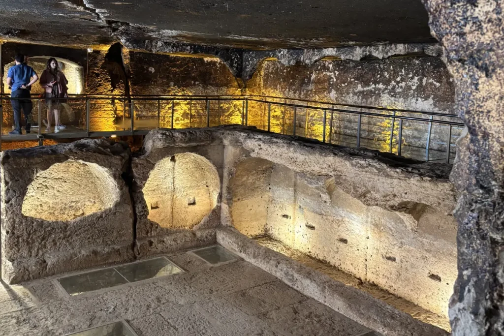 The interior of an ancient stone gallery grave in Dara, illuminated by golden light, showing multiple carved chambers.