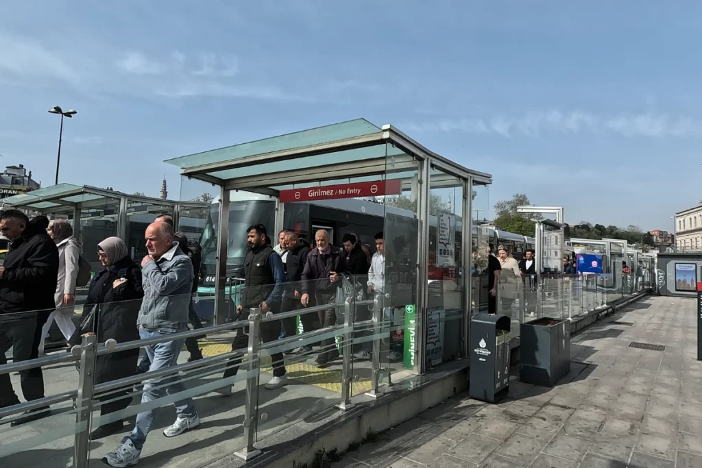 An outdoor tram stop platform in Istanbul with passengers waiting by the tracks next to signage.