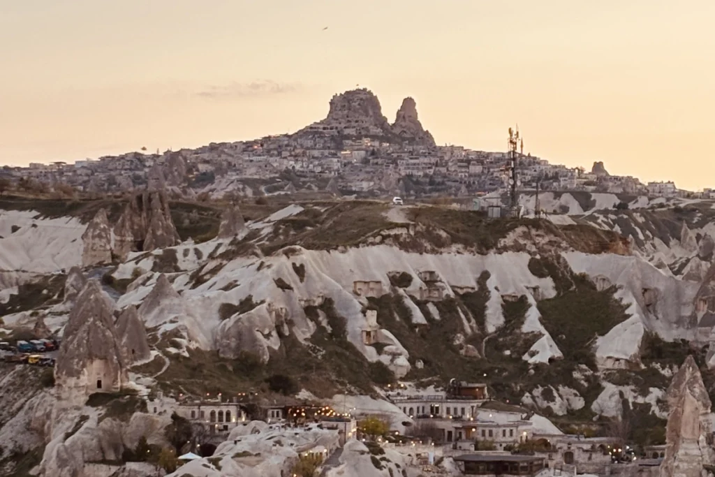 Uchiser Castle Silhouette of Göreme's rock formations and town buildings against a warm orange-and-blue dusk sky.