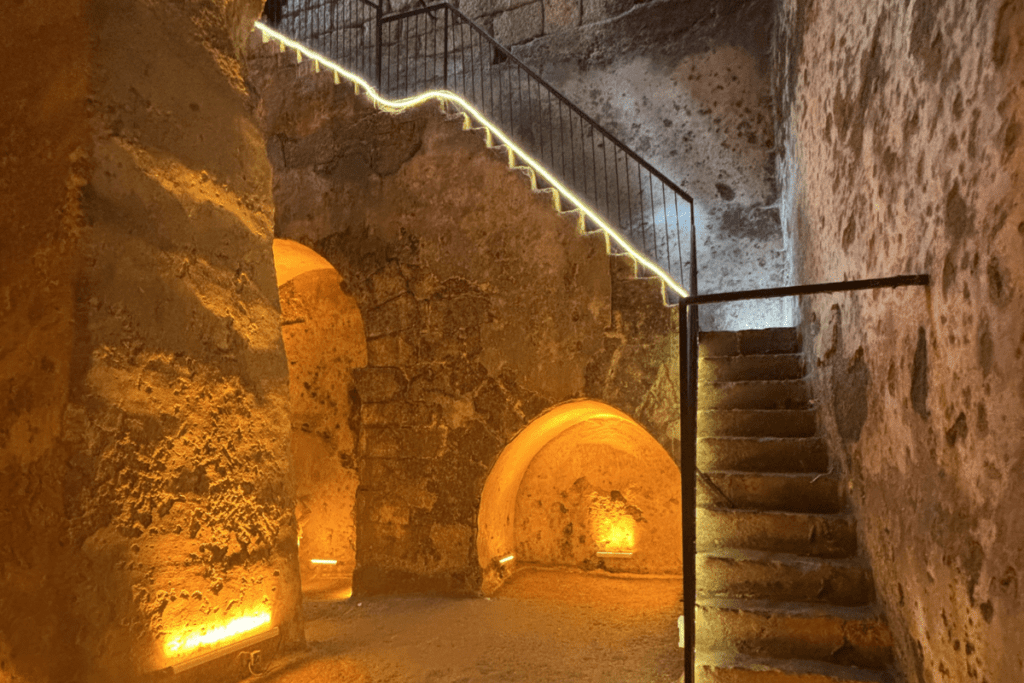 A metal staircase with railings leading down into a dimly lit underground stone cistern.