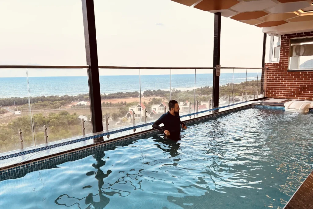Akash swimming in a clear blue rooftop infinity pool overlooking a city landscape.