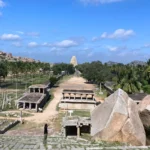 A wide panoramic view overlooking the ruined stone structures of the ancient bazaar market path leading towards the tall Virupaksha Temple gopuram tower in Hampi.