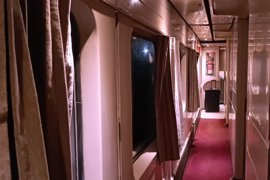 The inside of Watania sleeper train compartment, showing a made bed with white linens and a window looking out onto the landscape.