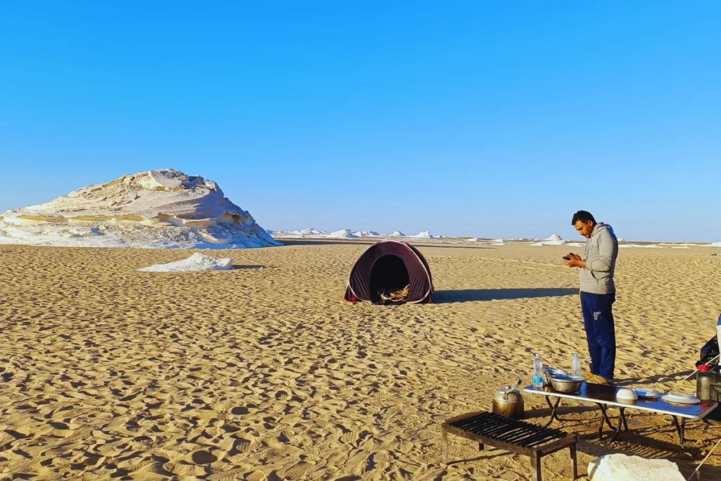 A single dome tent pitched on flat desert ground, with a guide standing nearby under a clear sky.