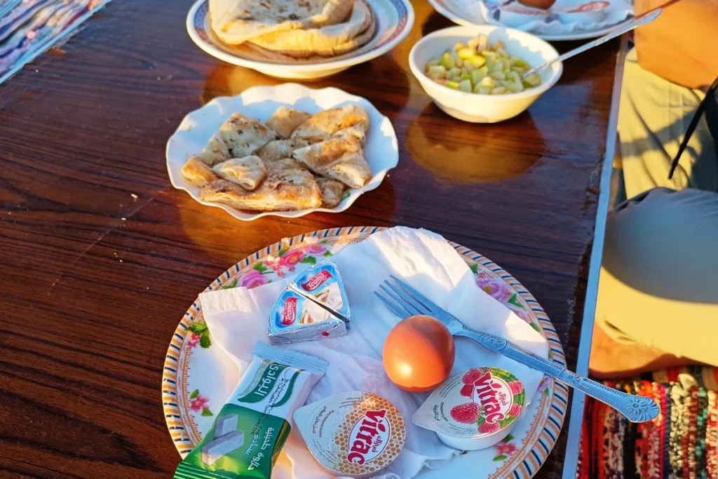 A colorful breakfast spread with tea, cheese, and bread set up on a blanket on the desert floor next to a rock.