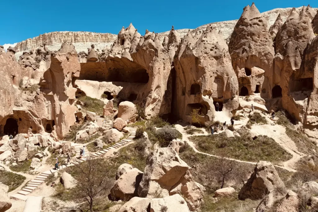 A rugged hillside dotted with numerous dark, hand-carved window and door openings leading into ancient subterranean cave dwellings.