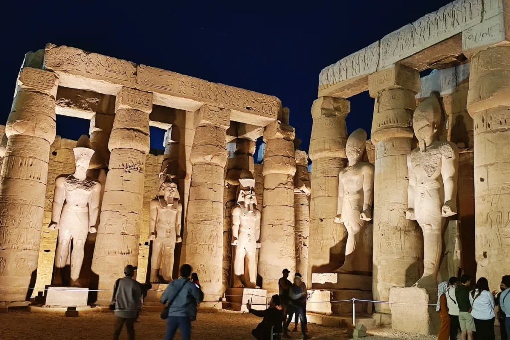  Giant illuminated stone statues standing guard at the gateway of Luxor Temple at night.