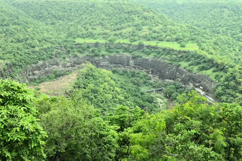 Ajanta Cave 1 A panoramic landscape view of the lush, horseshoe-shaped gorge surrounded by green hills, where the ancient Ajanta Caves are carved into the cliff face.