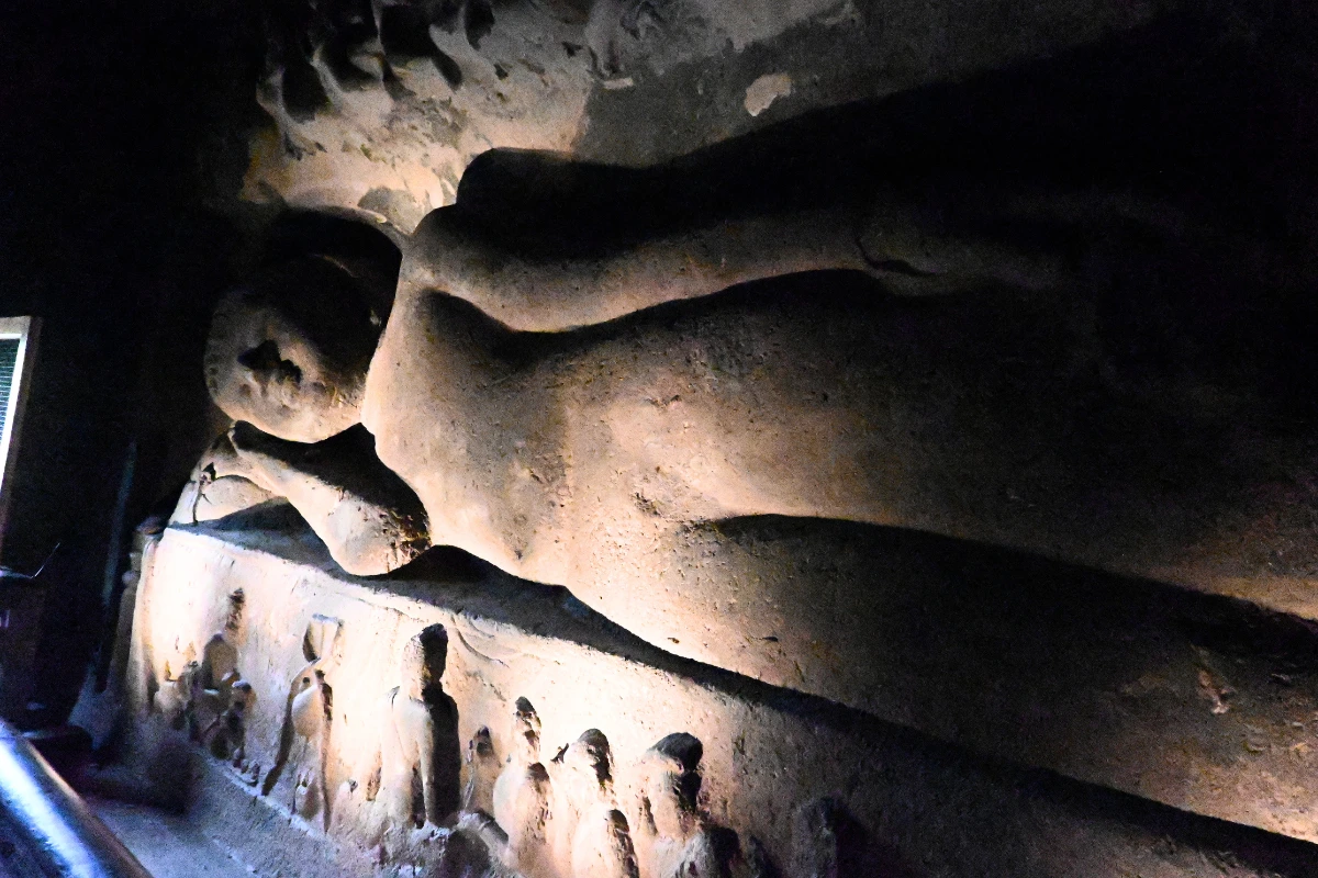 A close-up side view of the large stone-carved reclining Buddha statue inside Cave 26 at Ajanta Caves, illuminated by soft indoor lighting.