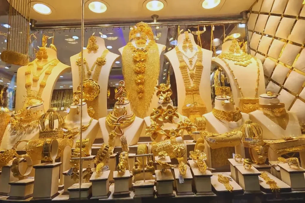Dubai- Gold A well-lit display window inside a jewelry store showcasing heavy, intricate gold necklaces, rings, and large ornamental pieces.