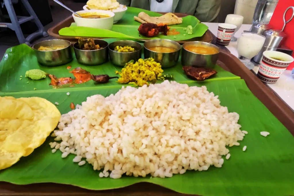 Dubai- food bowl- Kerala thali A top-down view of a massive mound of rice on a large banana leaf, surrounded by multiple small bowls filled with various Indian curries, side dishes, and accompaniments.