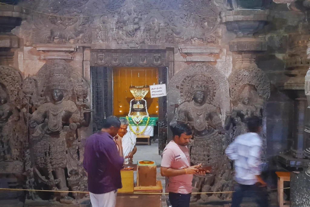 Hoysalaswar Temple 5 Visitors standing inside the dimly lit sanctum sanctorum in front of an illuminated Shiva Linga shrine.