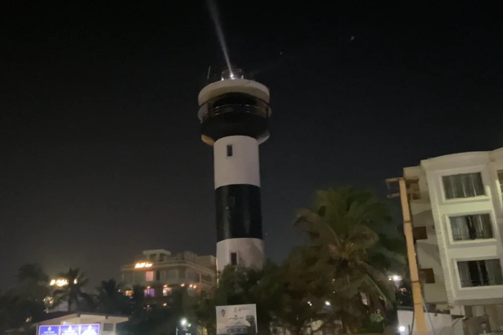 PURI NIGHT LIGHT HOUSE A nighttime shot of the tall black and white lighthouse illuminated by streetlights, with nearby hotel buildings visible.