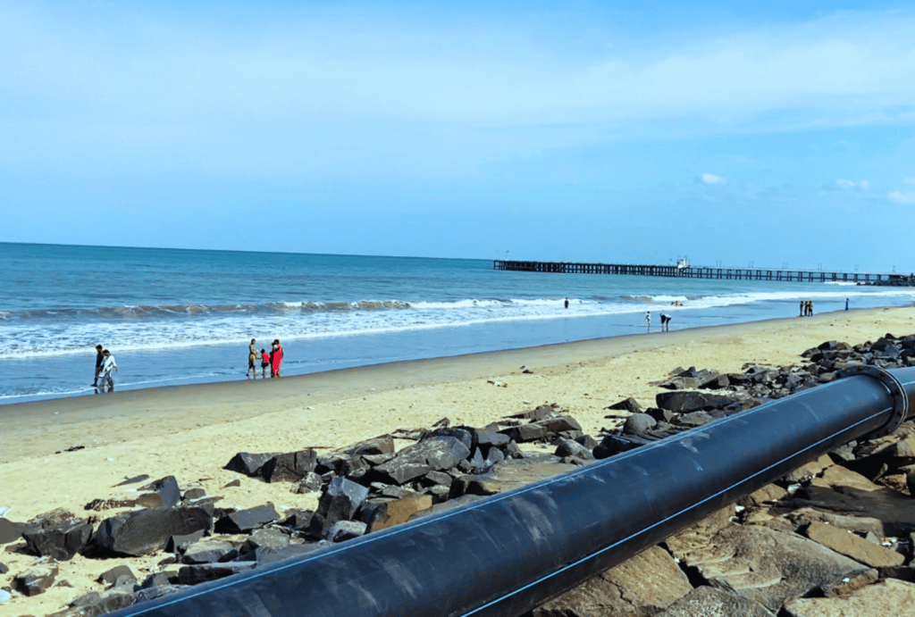 Pondicherry 2 A view across a rocky barrier wall lining a dark sand beach with blue ocean waters stretching into the distance.