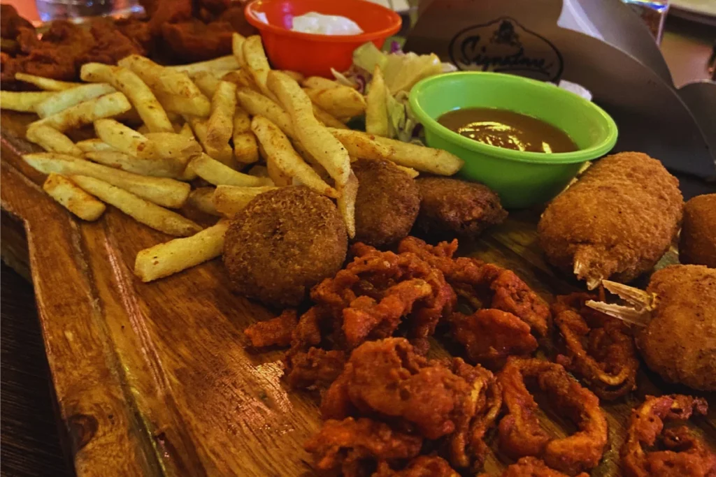 Pondicherry-Sea Food Platter A plate filled with golden-brown fried snacks, French fries, and a dipping sauce.